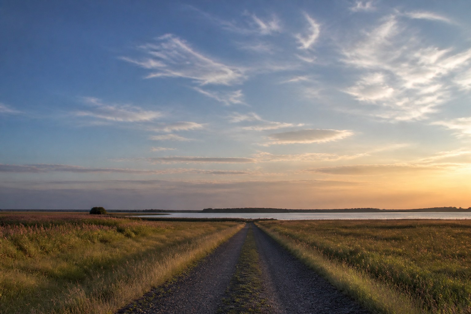 A long gravel track toward a silver lake under a huge northern sky, suggesting a multi-day crossing